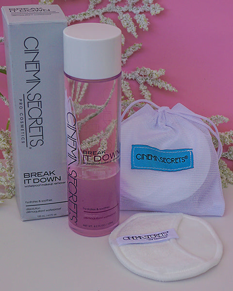 A white bag of cotton pads and a bottle of skin care on a table with a pink background