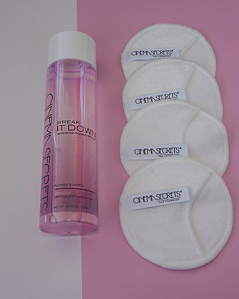 Four cotton pads and a bottle of skin care on a table with a pink adnd white background