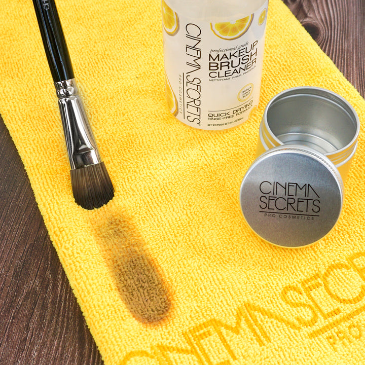 Yellow towel layed flat with metal tin ;emon brush cleaner and makeup brush on brown wood background