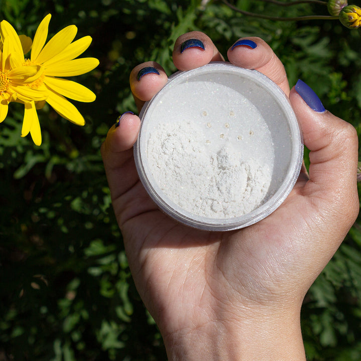 hand holding open container of highlight powder over grass