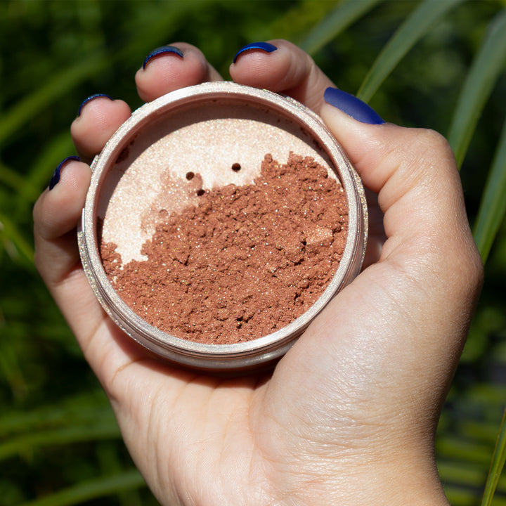 hand holding open container of highlight powder over grass